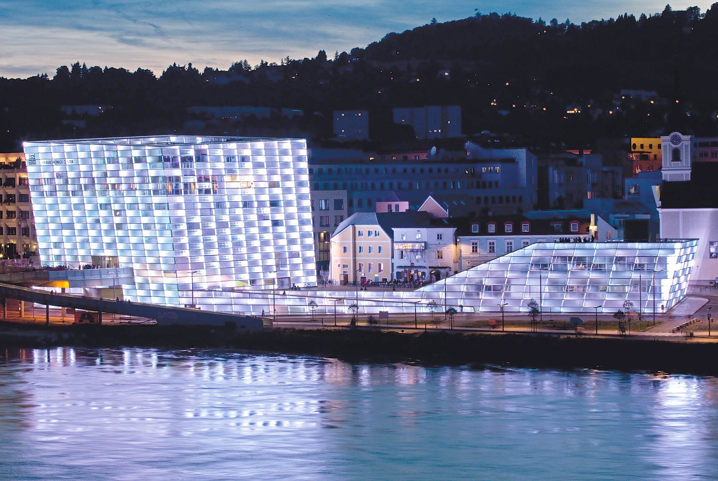 Blick auf den weiß ausgeleuchteten Ars Electronica Komplex vom gegenüberliegenden Donauufer.