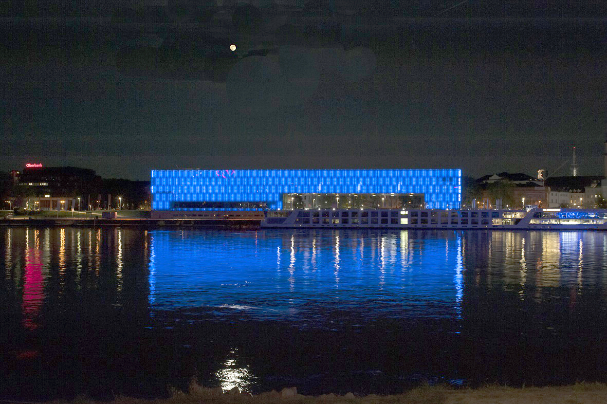 Foto des blau ausgeleuchteten Lentos Kunstmuseums vom gegenüberliegenden Donauufer.