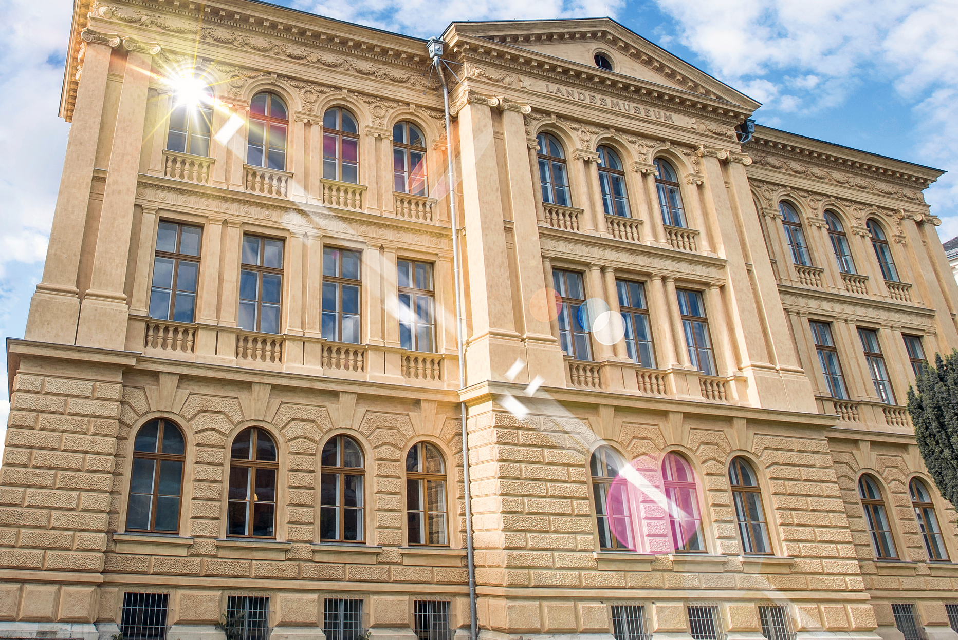 Foto des Landesmuseums Kärnten. Das erste Fenster im obersten Stock reflektiert die an einem heiteren Tag scheinende Sonne in die Kamera.