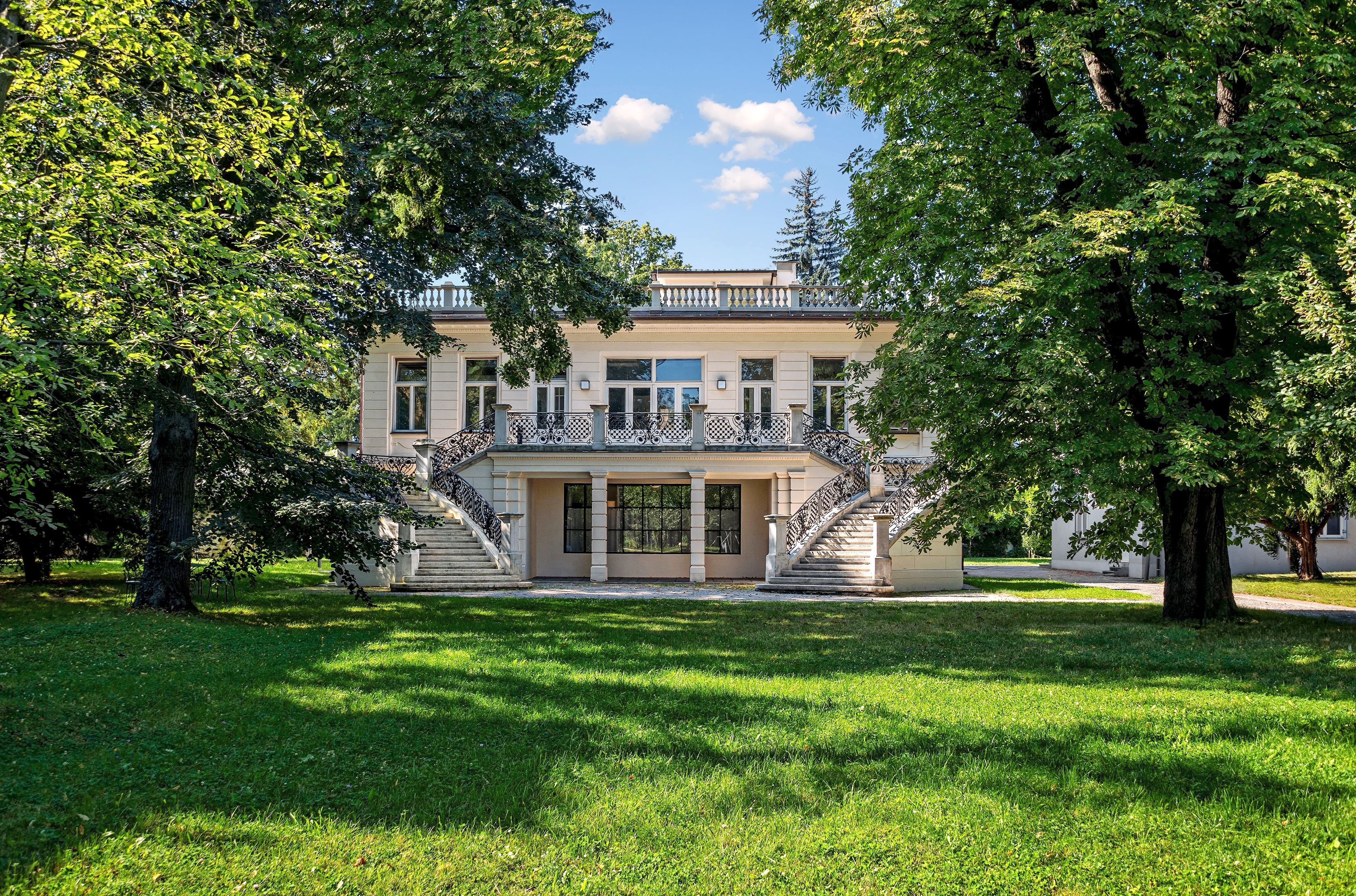 Blick vom grünen Garten auf die von zwei großen Bäumen umrahmte Klimt Villa.