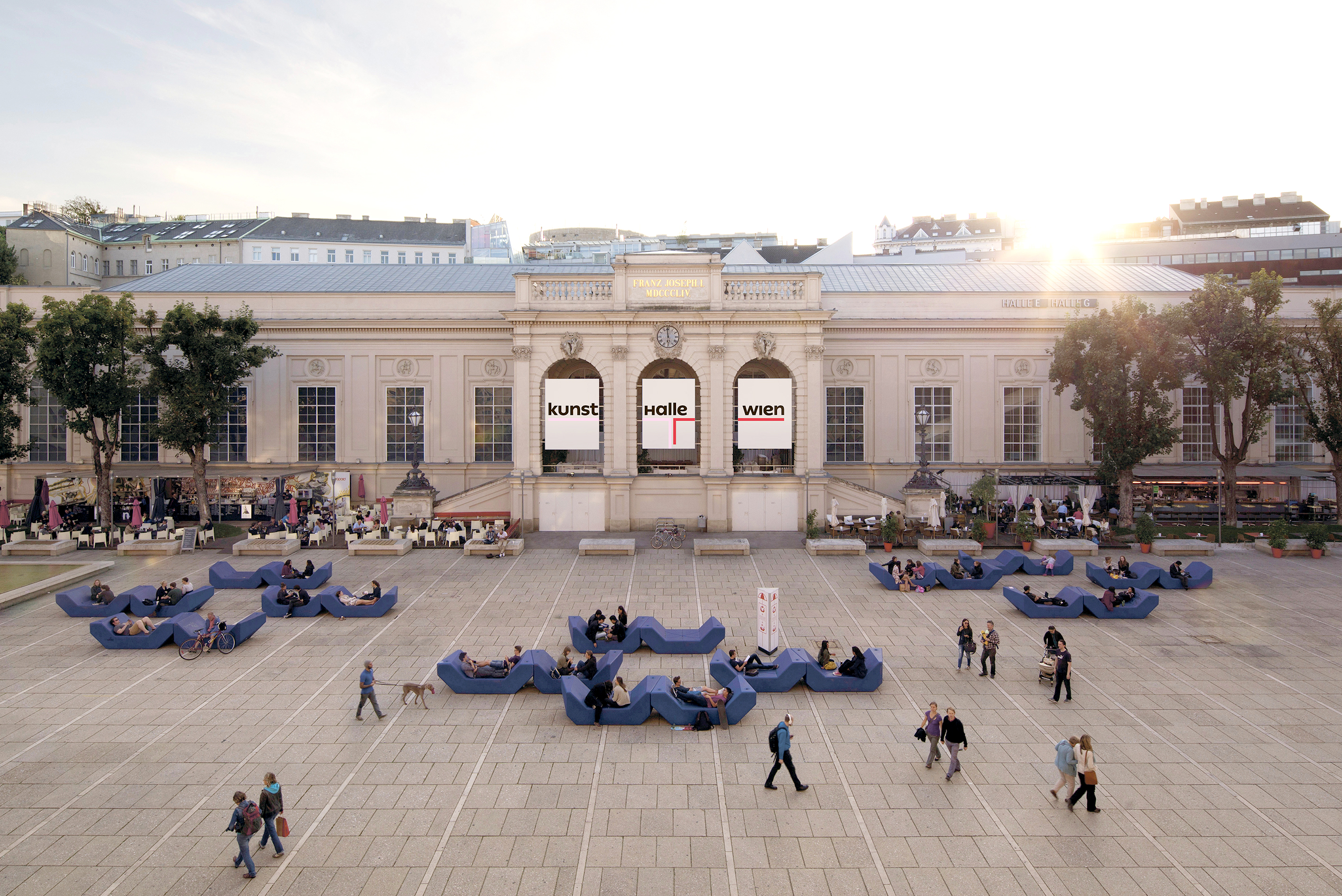 Blick auf die Kunsthalle Wien sowie den belebten Vorplatz bei strahlender Abendsonne.