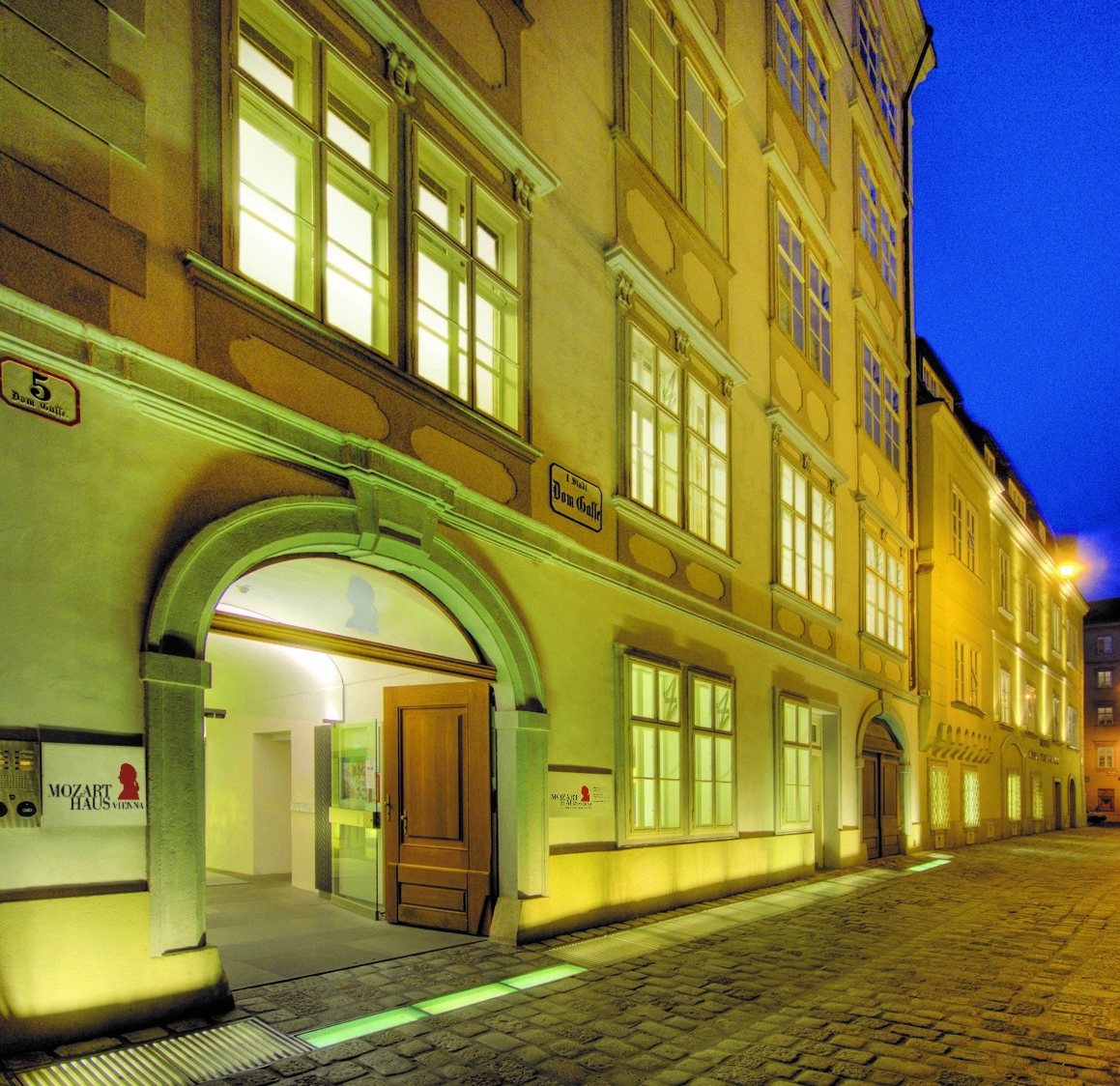 Fassade, Eingang und Teile der Gasse des Mozarthauses Vienna bei Nachtbeleuchtung.