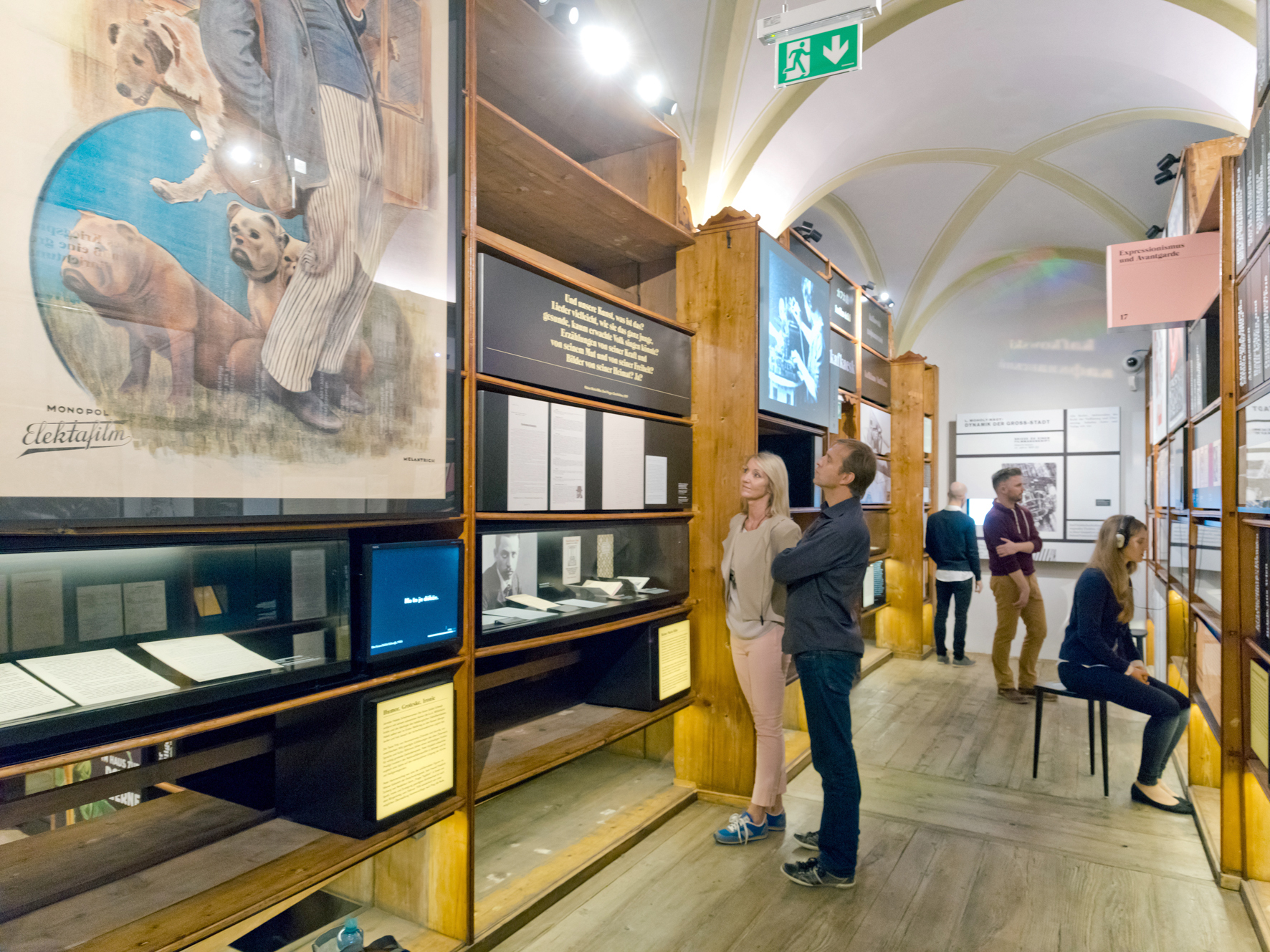 Mehrere Menschen betrachten diverse Ausstellungsobjekte in einem Ausstellungsraum des Literaturmuseums der Österreichischen Nationalbibliothek.