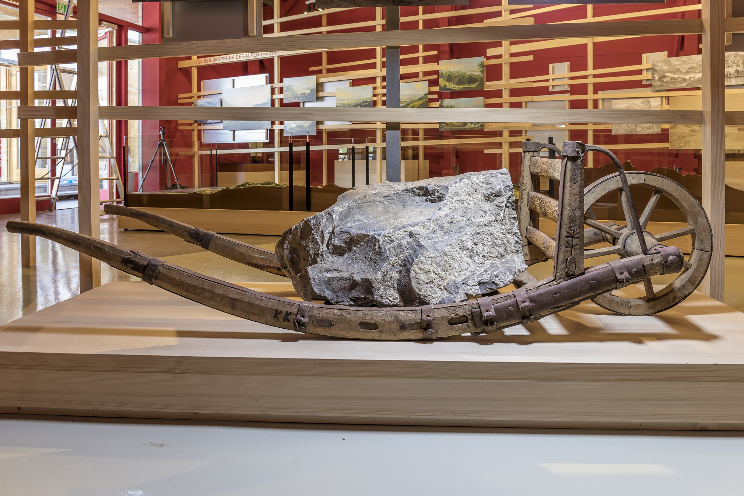 Mit Felsbrocken beladener historischer Holzkarren auf Ausstellungsplattform.