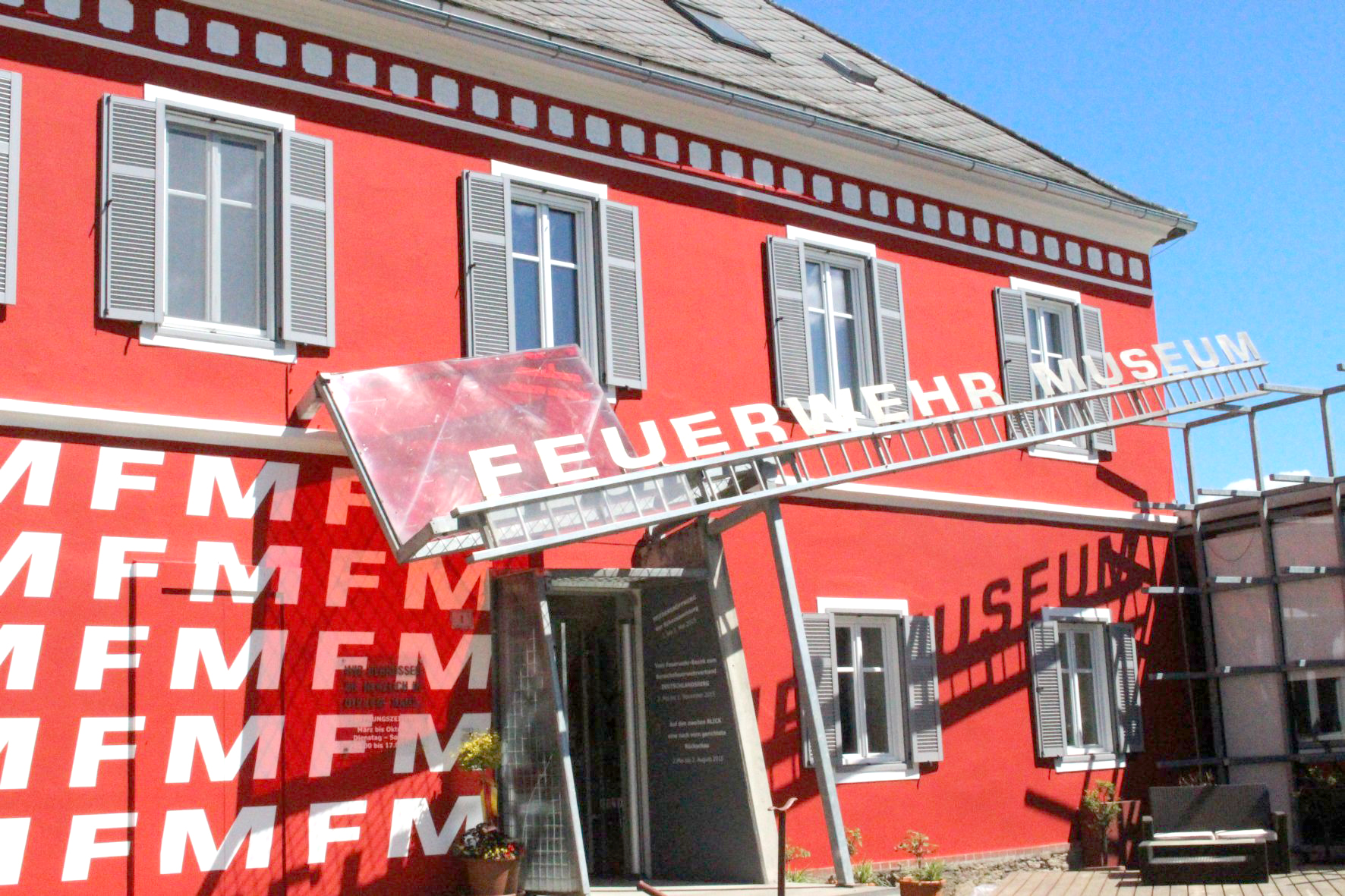 Foto des roten Gebäudes des Steirischen Feuerwehrmuseums. Über dem Eingang ist der auf einer Feuerwehrleiter sitzende Schriftzug "Feuerwehr Museum" angebracht.
