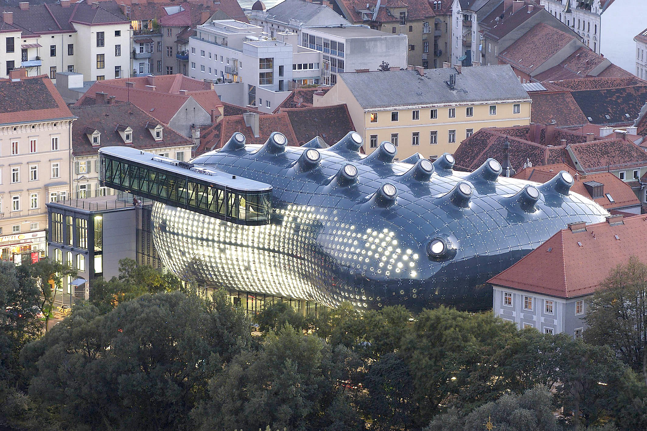 Foto des Kunsthauses Graz. Das Bauwerk, das auch unter dem Namen „Friendly Alien“ bekannt ist, hebt sich in Form und Material durch seine biomorphen, runden Formen bewusst von der barocken Dachlandschaft mit ihren roten Ziegeldächern ab. Stilistisch ist das Kunsthaus Graz der Blob-Architektur zuzuordnen.