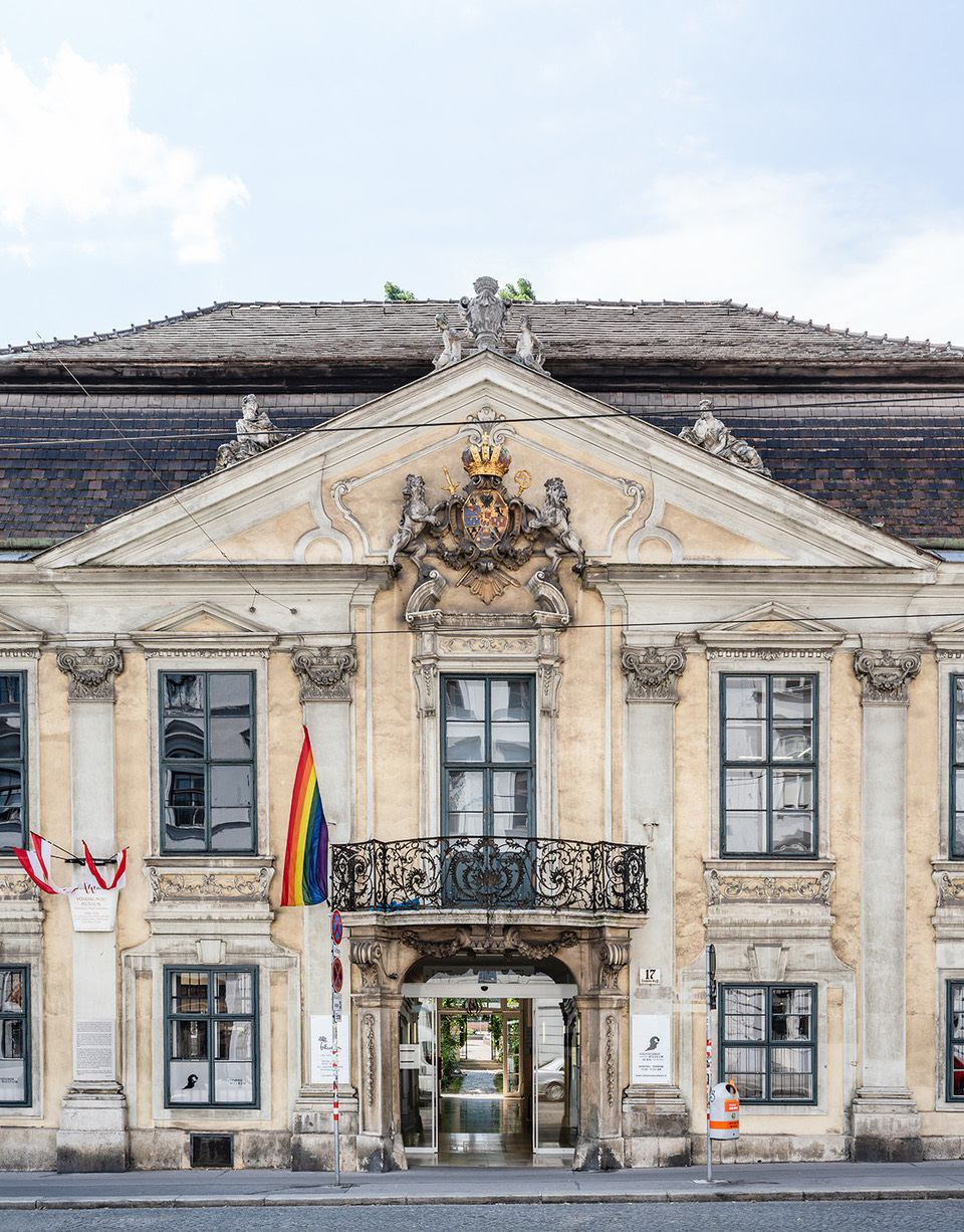 Foto der Fassade des Volkskundemuseums Wien. Vom Balkon weht eine Regenbogenfahne.