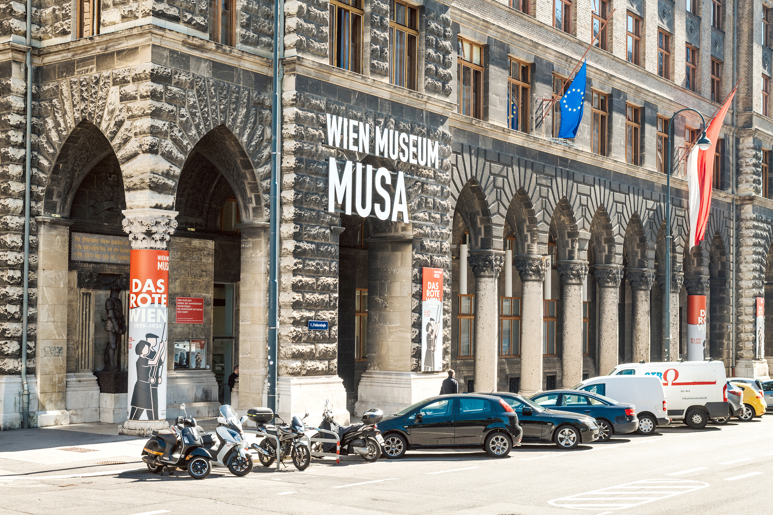 Foto der Fassade des Wien Museums MUSA und mehrerer davor geparkter Fahrzeuge.