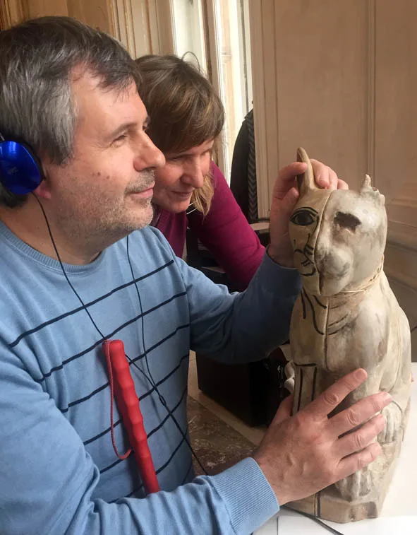 Foto von einem Mann mit Blindenstock und einer Frau, die im Manchester Museum eine 3D-Replik einer Katzenstatue ertasten.