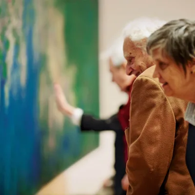 Foto von einer Gruppe älterer Besucher vor einem Gemälde von Claude Monet im Museum of Modern Art, New York. Das Gemälde wird von Blau- und Grüntönen dominiert. Ein Motiv ist auf dem Foto nicht erkennbar.