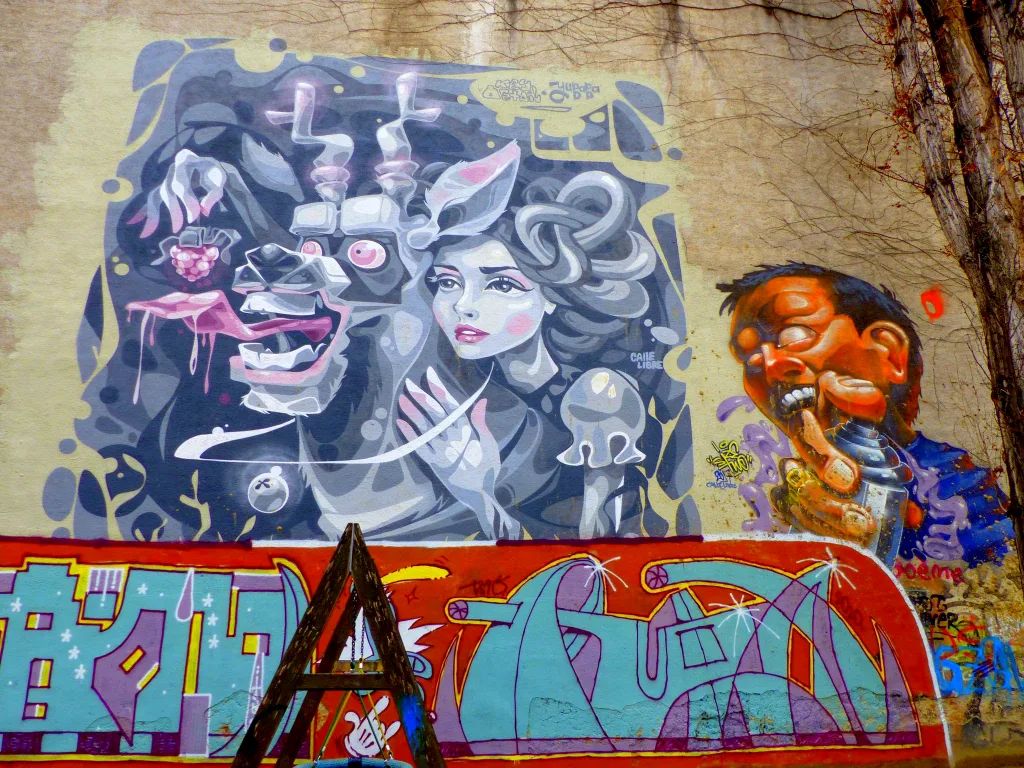 Foto eines weitgehend in Grau- und Rosatönen gehaltenen Graffitis am Karl-Farkas-Platz im 7. Wiener Gemeinebezirk. Abgebildet sind das Gesicht und die Hände einer jungen Frau, die ein hirschartiges Tier mit einer Beere füttert.