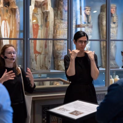 Eine Museumsführerin und eine Gebärdensprachdolmetscherin vor antiken ägyptischen Sarkophagen