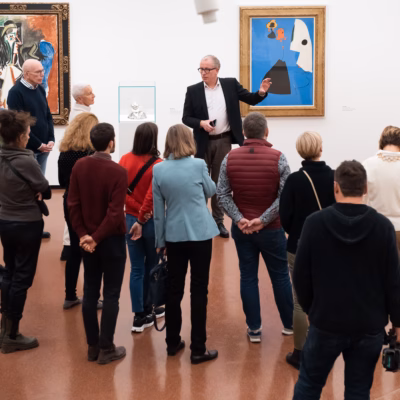 Ein Museumsführer erklärt einer Gruppe von Besuchern vor Kunstwerken die Ausstellung